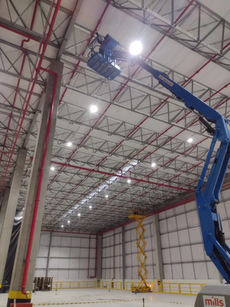 Grande galpão com plataforma elevatória realizando instalação de sprinklers que são essenciais em projetos de Engenharia de Incêndio