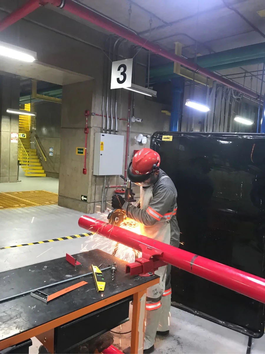 Técnico soldando tubulação vermelha em ambiente industrial